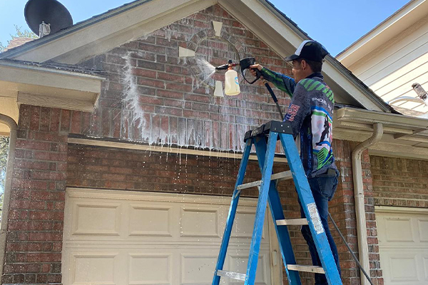 A Biocleaners USA employee, standing on a ladder, cleans the entrance to a residential garage, using pressure washing equipment.