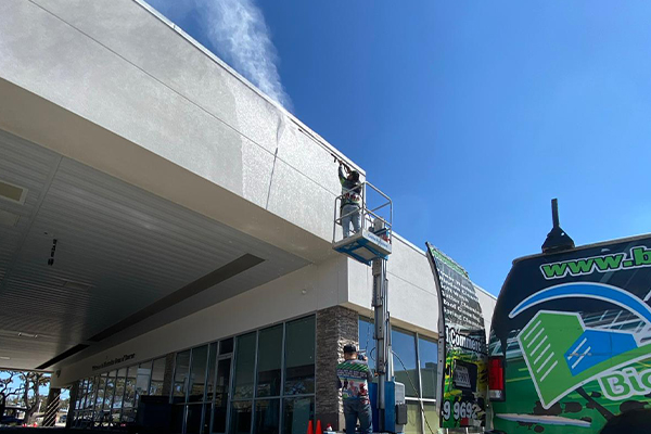 A Biocleaners USA employee, elevated on a crane, cleans the highest part of a commercial building using pressure washing equipment.