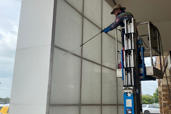 A Biocleaners worker on a ladder, using machinery to clean a structure in a commercial building with the softwashing technique