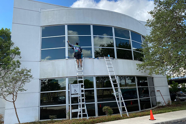 A man on a ladder cleaning a window on a second floor.